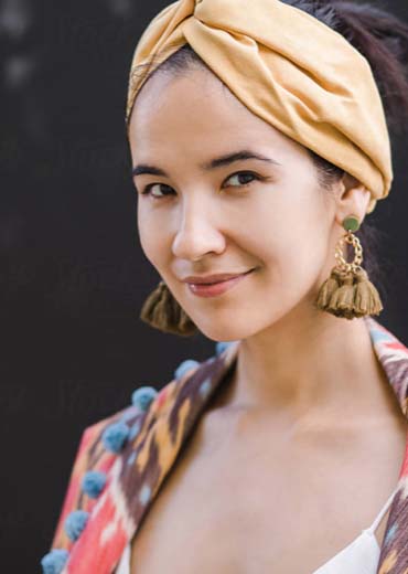 A woman wearing a yellow headscarf and tassel earrings in a vibrant outfit.